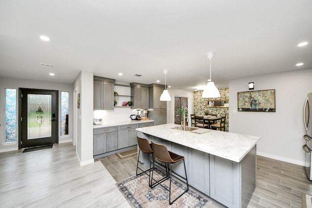 6803 Las Brisas Dr, Houston, TX 77083 - kitchen with gray cabinetry, open shelves, light wood-type flooring, recessed lighting, and a center island with sink