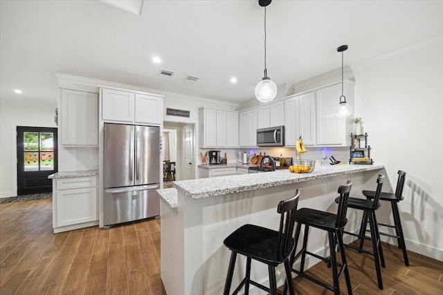 2201 Maple St, Liberty, TX 77575 - kitchen featuring appliances with stainless steel finishes, a peninsula, wood finished floors, ornamental molding, and white cabinetry