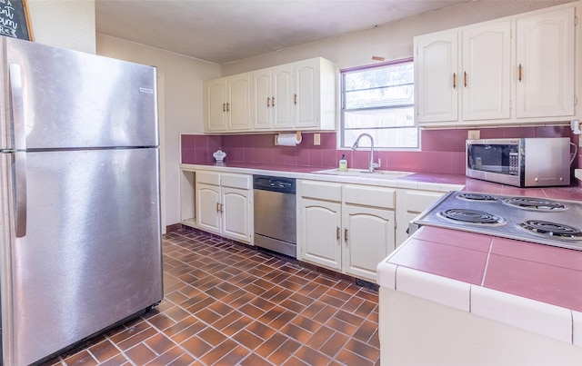 7734 El Rancho St, Houston, TX 77087 - kitchen with appliances with stainless steel finishes, tile counters, white cabinets, brick patterned flooring, and decorative backsplash