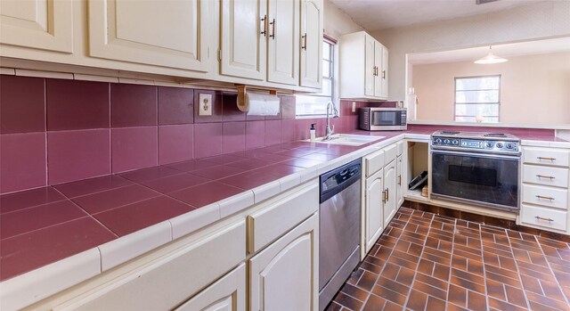 7734 El Rancho St, Houston, TX 77087 - kitchen featuring appliances with stainless steel finishes, backsplash, tile countertops, brick patterned flooring, and white cabinetry