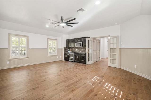 10332 Hunter Creek Ln, Conroe, TX 77304 - unfurnished living room featuring beverage cooler, a wainscoted wall, light wood-type flooring, a ceiling fan, and bar