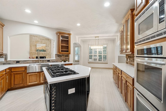 10332 Hunter Creek Ln, Conroe, TX 77304 - kitchen with stainless steel appliances, brown cabinetry, tasteful backsplash, a center island, and glass insert cabinets