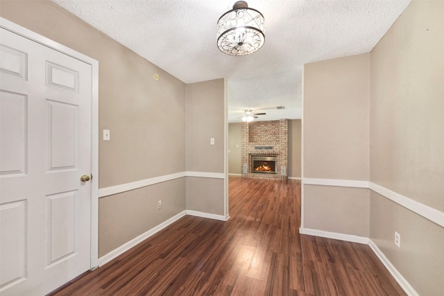 1002 Williams St, Cleveland, TX 77327 - unfurnished living room featuring a textured ceiling, dark wood-style flooring, a ceiling fan, a brick fireplace, and a chandelier