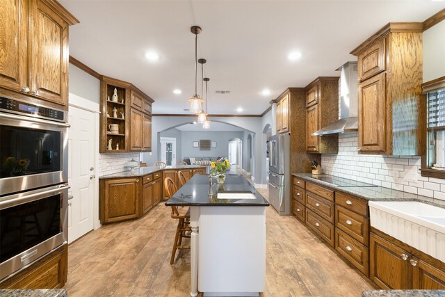 194 2 Mile Ln, Smithville, TX 78957 - kitchen with appliances with stainless steel finishes, wall chimney range hood, arched walkways, brown cabinetry, and a kitchen bar