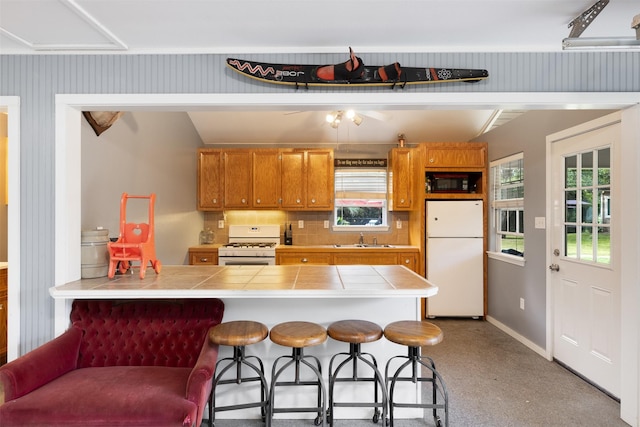 194 2 Mile Ln, Smithville, TX 78957 - kitchen with white appliances, tile countertops, brown cabinetry, a breakfast bar area, and a peninsula
