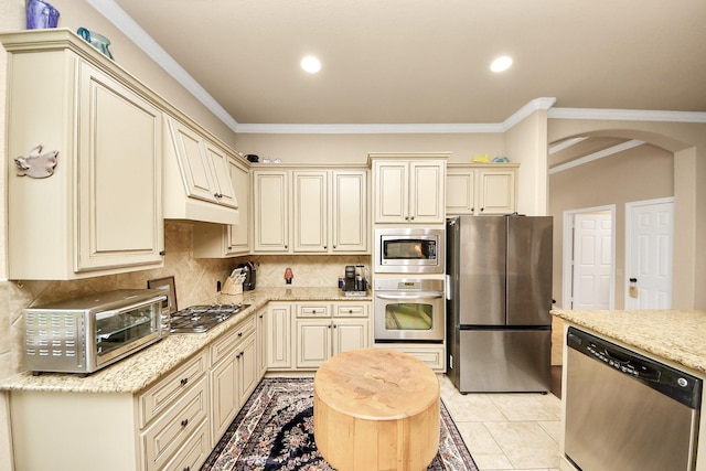 9419 Pecos Pass Ct, Cypress, TX 77433 - kitchen with appliances with stainless steel finishes, cream cabinetry, arched walkways, backsplash, and light stone countertops