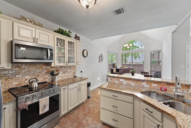 3330 Lake Island Dr, Montgomery, TX 77356 - kitchen with appliances with stainless steel finishes, vaulted ceiling, decorative backsplash, cream cabinetry, and light stone counters
