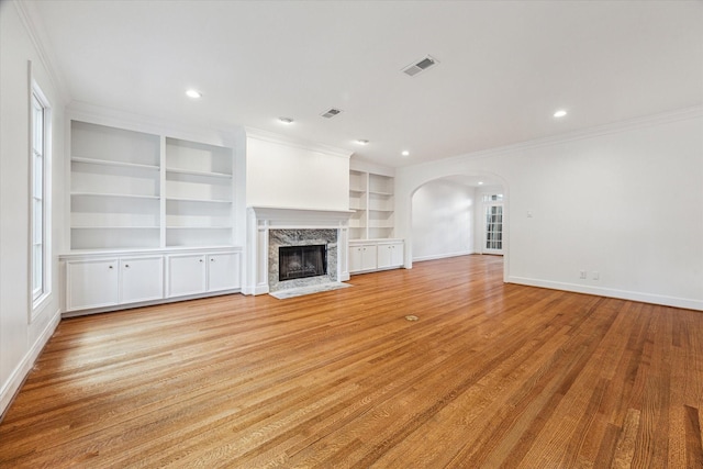 1976 Vermont St, Houston, TX 77019 - unfurnished living room featuring crown molding, arched walkways, built in shelves, light wood-style floors, and a high end fireplace