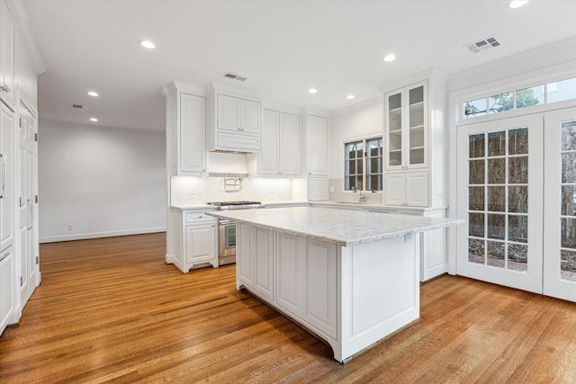 1976 Vermont St, Houston, TX 77019 - kitchen featuring stainless steel stove, light wood finished floors, white cabinetry, tasteful backsplash, and recessed lighting