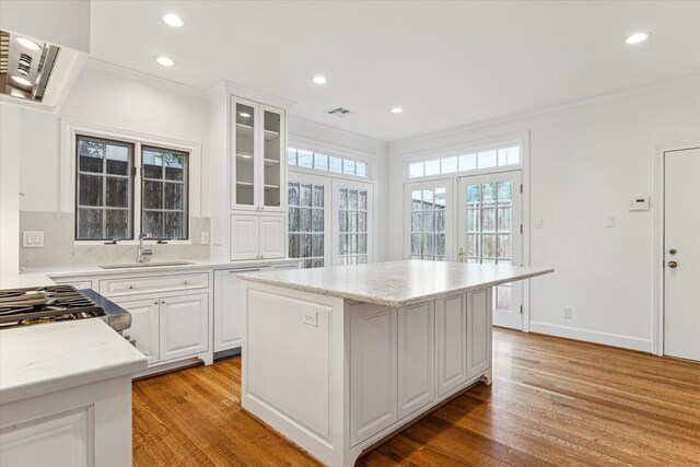 1976 Vermont St, Houston, TX 77019 - kitchen featuring light wood-style floors, ornamental molding, a center island, recessed lighting, and glass insert cabinets
