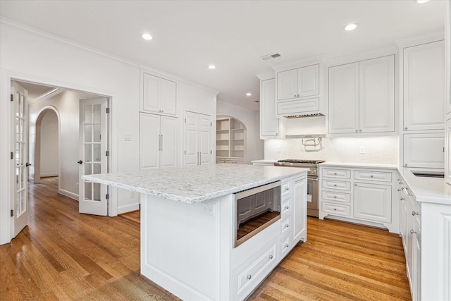 1976 Vermont St, Houston, TX 77019 - kitchen featuring arched walkways, stainless steel appliances, ornamental molding, light wood-style floors, and a kitchen island