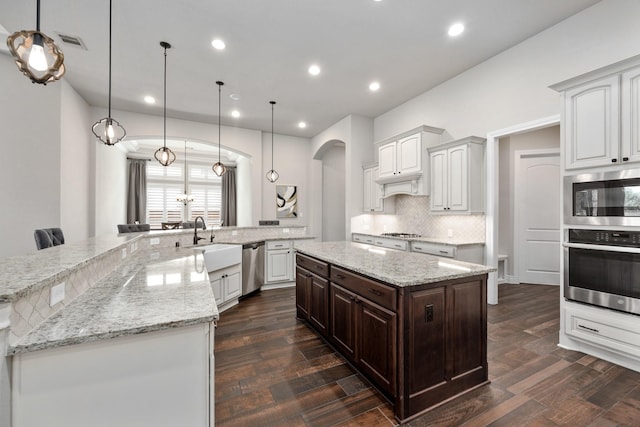 19219 Spotted Bass Ln, Cypress, TX 77433 - kitchen with stainless steel appliances, a large island, arched walkways, tasteful backsplash, and dark wood-style flooring