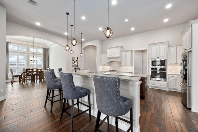 19219 Spotted Bass Ln, Cypress, TX 77433 - kitchen with stainless steel appliances, arched walkways, a spacious island, backsplash, and a breakfast bar