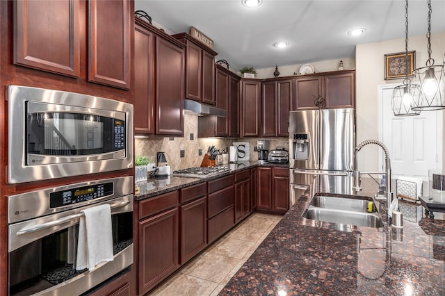 19334 St Winfred Dr, Spring, TX 77379 - kitchen with stainless steel appliances, under cabinet range hood, backsplash, dark stone counters, and decorative light fixtures