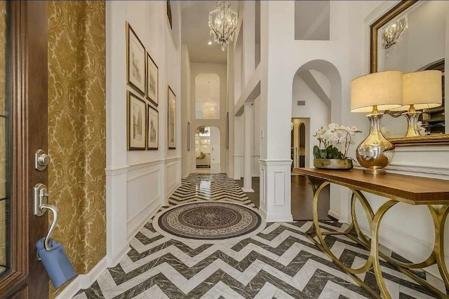 6423 Middlelake Ct, Katy, TX 77450 - hallway with inlaid floor details, a towering ceiling, a chandelier, arched walkways, and wainscoting