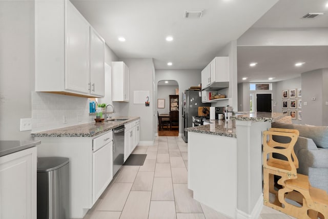 23803 Spring Way Dr, Spring, TX 77373 - kitchen featuring arched walkways, appliances with stainless steel finishes, stone counters, white cabinetry, and a kitchen bar