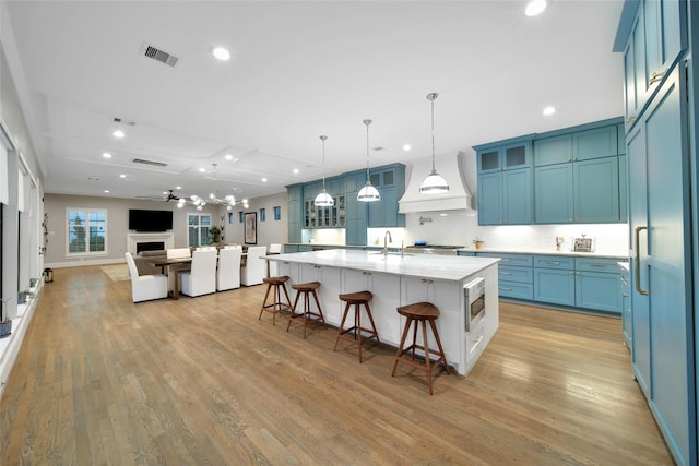 1353 Chantilly Ln, Houston, TX 77018 - kitchen featuring a kitchen bar, light wood-style flooring, glass insert cabinets, custom exhaust hood, and recessed lighting