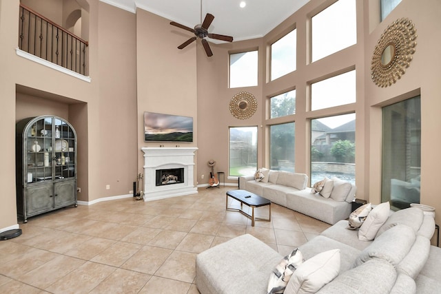 13723 Playa Lucia Ct, Houston, TX 77044 - living room featuring a high ceiling, a ceiling fan, a fireplace with raised hearth, light tile patterned floors, and crown molding