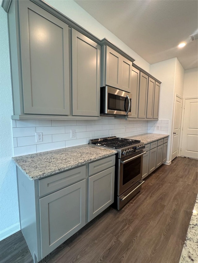 214 Fulton Station Dr, Houston, TX 77009 - kitchen with stainless steel appliances, dark wood finished floors, gray cabinets, decorative backsplash, and light stone countertops