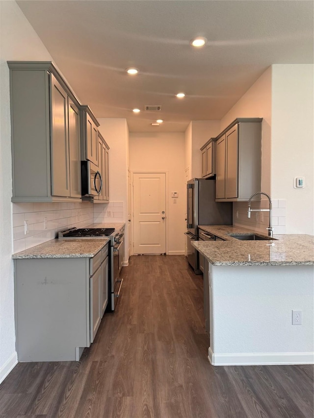 214 Fulton Station Dr, Houston, TX 77009 - kitchen with stainless steel appliances, light stone counters, dark wood-type flooring, decorative backsplash, and gray cabinetry