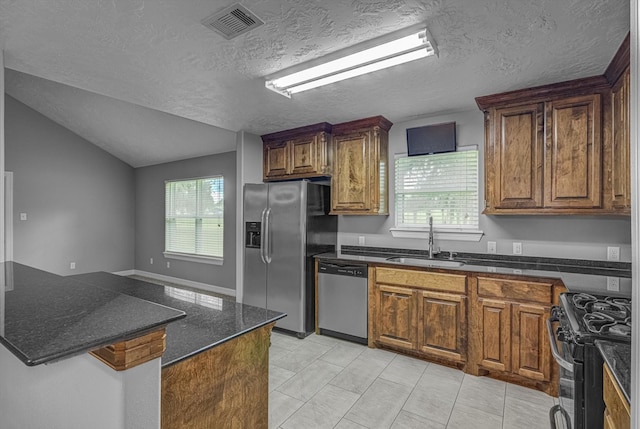 2440 Olympia Dr, West Columbia, TX 77486 - kitchen with stainless steel appliances, a textured ceiling, vaulted ceiling, brown cabinetry, and light tile patterned flooring