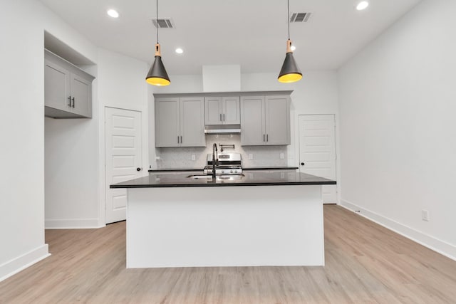 2213 Lee St, Houston, TX 77026 - kitchen with gray cabinetry, dark countertops, tasteful backsplash, under cabinet range hood, and light wood-style flooring