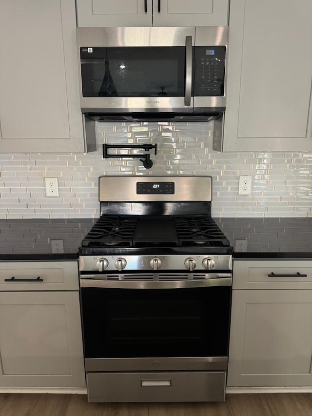 2213 Lee St, Houston, TX 77026 - kitchen with appliances with stainless steel finishes, dark countertops, wood finished floors, backsplash, and white cabinets