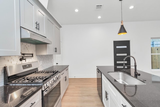 2213 Lee St, Houston, TX 77026 - kitchen featuring appliances with stainless steel finishes, under cabinet range hood, backsplash, dark stone countertops, and pendant lighting
