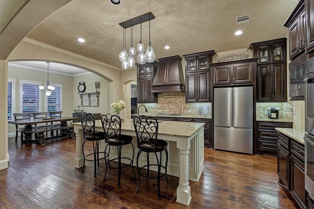 9714 Luna Springs Ln, Cypress, TX 77433 - kitchen featuring freestanding refrigerator, premium range hood, arched walkways, cooktop, and a chandelier