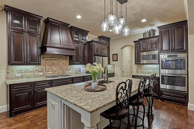 9714 Luna Springs Ln, Cypress, TX 77433 - kitchen with stainless steel appliances, premium range hood, arched walkways, dark brown cabinetry, and glass insert cabinets