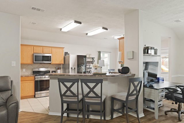 15010 Sunset Villa Ct, Humble, TX 77396 - kitchen with stainless steel appliances, a kitchen bar, decorative backsplash, and light wood-type flooring