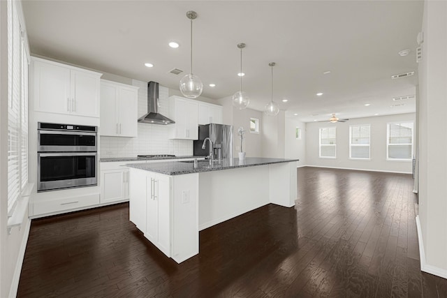 1909 Monaco Memorial Ln, Houston, TX 77043 - kitchen featuring wall chimney range hood, stainless steel appliances, a center island with sink, dark wood-style flooring, and recessed lighting