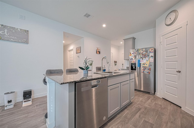 3918 Beltingham Bend Way, Fulshear, TX 77441 - kitchen with stainless steel appliances, gray cabinetry, light wood-style floors, dark stone countertops, and a kitchen island with sink