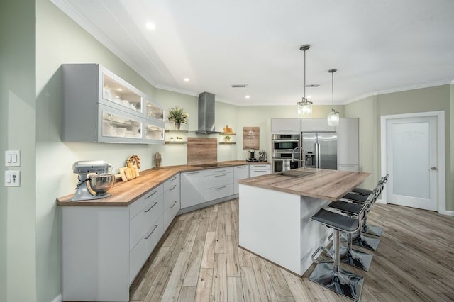 21215 Kelliwood Greens Dr, Katy, TX 77450 - kitchen with butcher block counters, wall chimney exhaust hood, appliances with stainless steel finishes, a kitchen bar, and ornamental molding