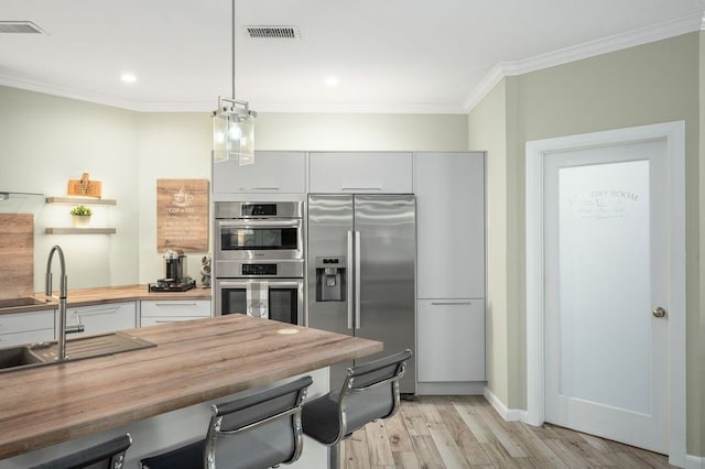 21215 Kelliwood Greens Dr, Katy, TX 77450 - kitchen with appliances with stainless steel finishes, butcher block countertops, light wood-style floors, ornamental molding, and decorative light fixtures