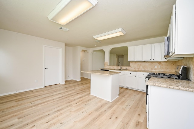 2046 Grand Park Dr, Missouri City, TX 77489 - kitchen featuring gas range, arched walkways, decorative backsplash, white cabinets, and light wood-style flooring