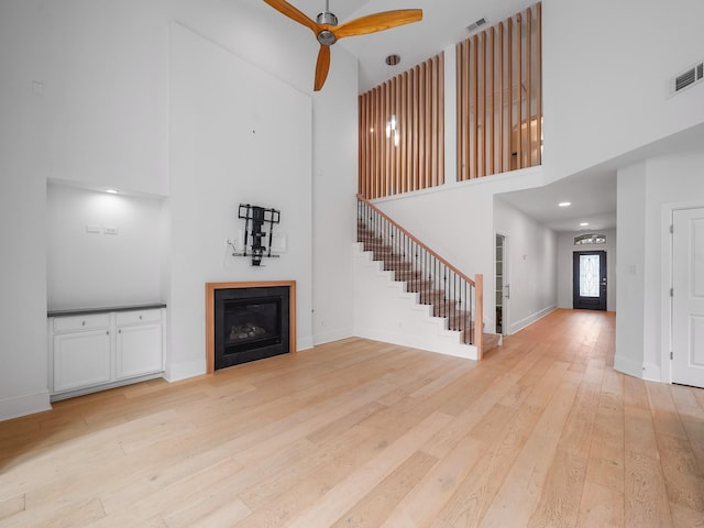 28111 Harper Creek Ln, Katy, TX 77494 - unfurnished living room featuring a towering ceiling, a ceiling fan, stairs, light wood-style floors, and a glass covered fireplace