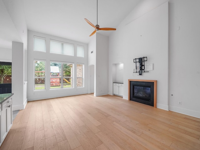 28111 Harper Creek Ln, Katy, TX 77494 - unfurnished living room featuring high vaulted ceiling, a glass covered fireplace, light wood-style floors, and ceiling fan