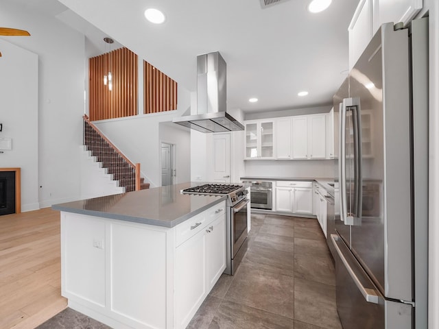 28111 Harper Creek Ln, Katy, TX 77494 - kitchen with stainless steel appliances, wall chimney range hood, a center island, glass insert cabinets, and white cabinetry