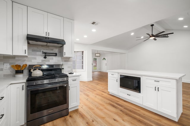 9030 Tanager St, Houston, TX 77036 - kitchen featuring stainless steel gas range oven, under cabinet range hood, black microwave, decorative backsplash, and light wood-style floors
