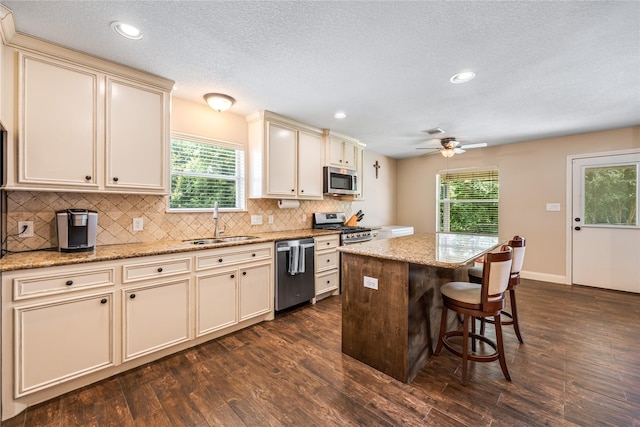 2546 Anzalone Dr, Spring, TX 77373 - kitchen featuring appliances with stainless steel finishes, cream cabinets, dark wood-style floors, backsplash, and a center island