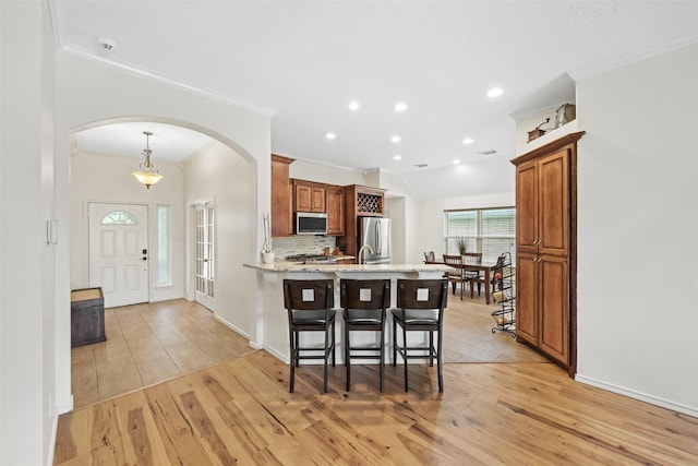 5207 Caprock Dr, Pearland, TX 77584 - kitchen featuring stainless steel appliances, arched walkways, a peninsula, light wood-style flooring, and ornamental molding