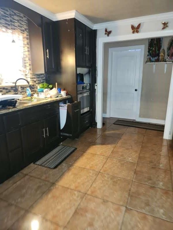 1902 July St, Houston, TX 77093 - kitchen featuring dark cabinetry, light tile patterned floors, backsplash, crown molding, and light countertops