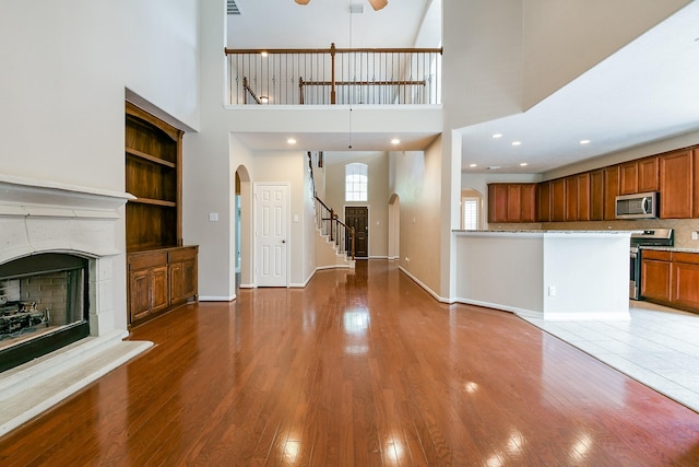 14307 Baron Creek Ln, Houston, TX 77044 - unfurnished living room with arched walkways, a ceiling fan, a fireplace with raised hearth, wood finished floors, and a high ceiling