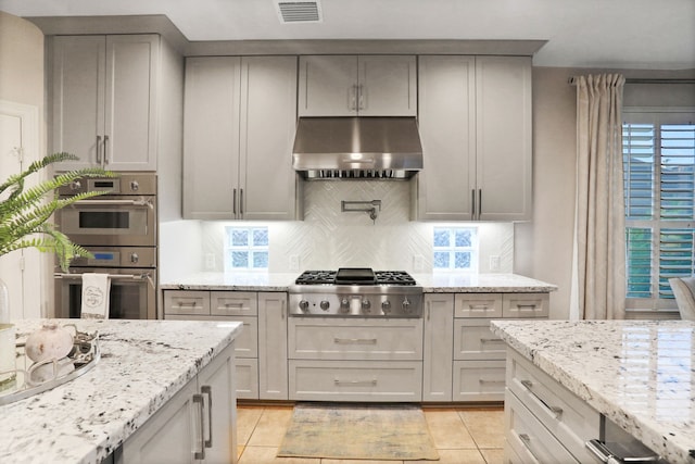 4502 Buffalo Lake Ct, Richmond, TX 77406 - kitchen with stainless steel appliances, under cabinet range hood, backsplash, gray cabinetry, and light stone countertops