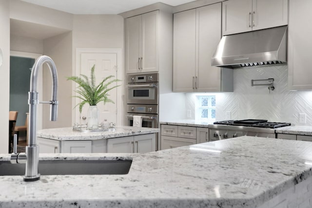4502 Buffalo Lake Ct, Richmond, TX 77406 - kitchen with under cabinet range hood, stainless steel appliances, decorative backsplash, light stone counters, and gray cabinets