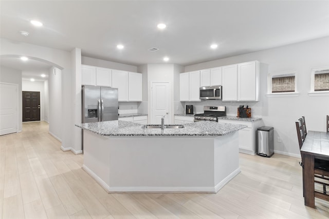 214 Water Grass Trl, Clute, TX 77531 - kitchen featuring stainless steel appliances, arched walkways, a center island with sink, light stone countertops, and light wood finished floors