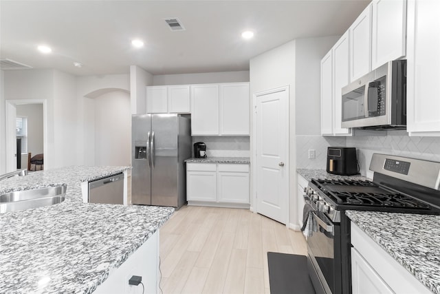 214 Water Grass Trl, Clute, TX 77531 - kitchen with appliances with stainless steel finishes, arched walkways, white cabinetry, backsplash, and light stone counters