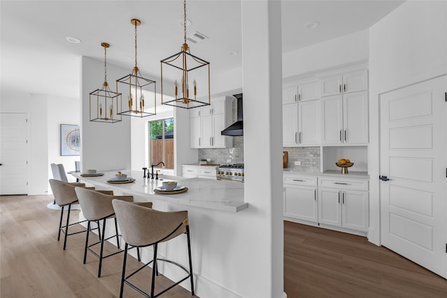2031 Peppermill Rd, Houston, TX 77080 - kitchen featuring wall chimney exhaust hood, light wood-style flooring, a chandelier, a breakfast bar, and white cabinetry