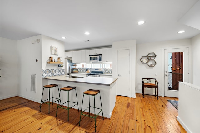 1821 Tuam St, Houston, TX 77004 - kitchen featuring stainless steel appliances, a peninsula, a kitchen bar, white cabinets, and light wood-style flooring